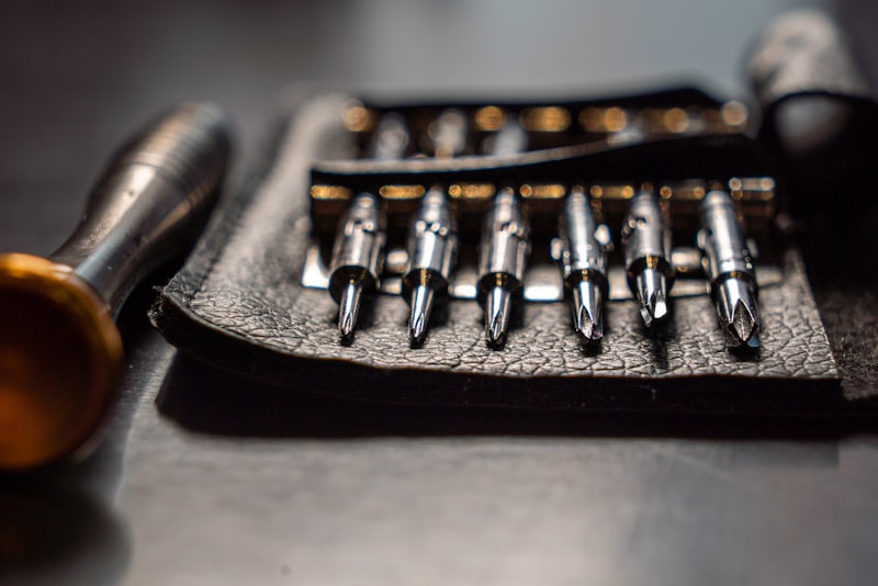 A small set of hand tools, caulk, and a putty knife laid out on a wooden surface